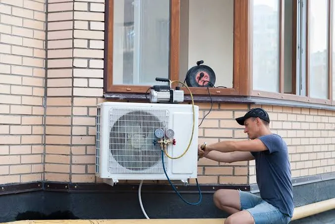 Technician connecting gauges to a wall-mounted outdoor cooling unit