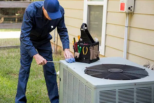 HVAC technician servicing a residential outdoor condenser beside a home